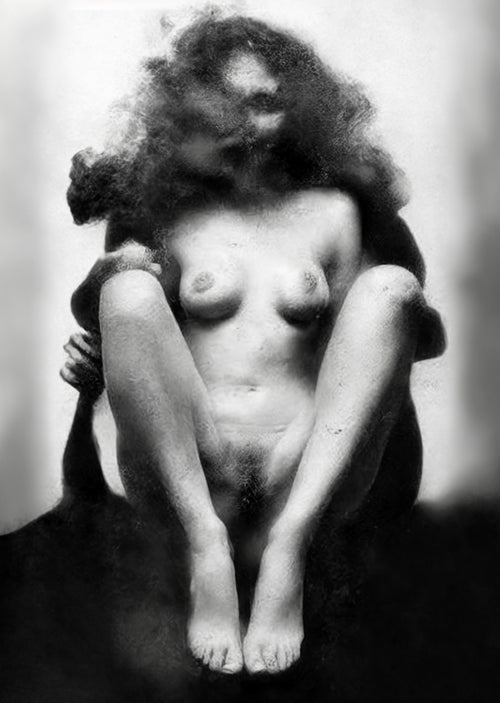 Black and white artistic photograph of a nude woman seated with her legs bent, surrounded by smoke or fog against a light studio background. Unmoored series.
