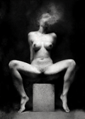 Black and white fine art photograph of a nude female figure seated on a rectangular pedestal against a dark textured background. Unmoored series.