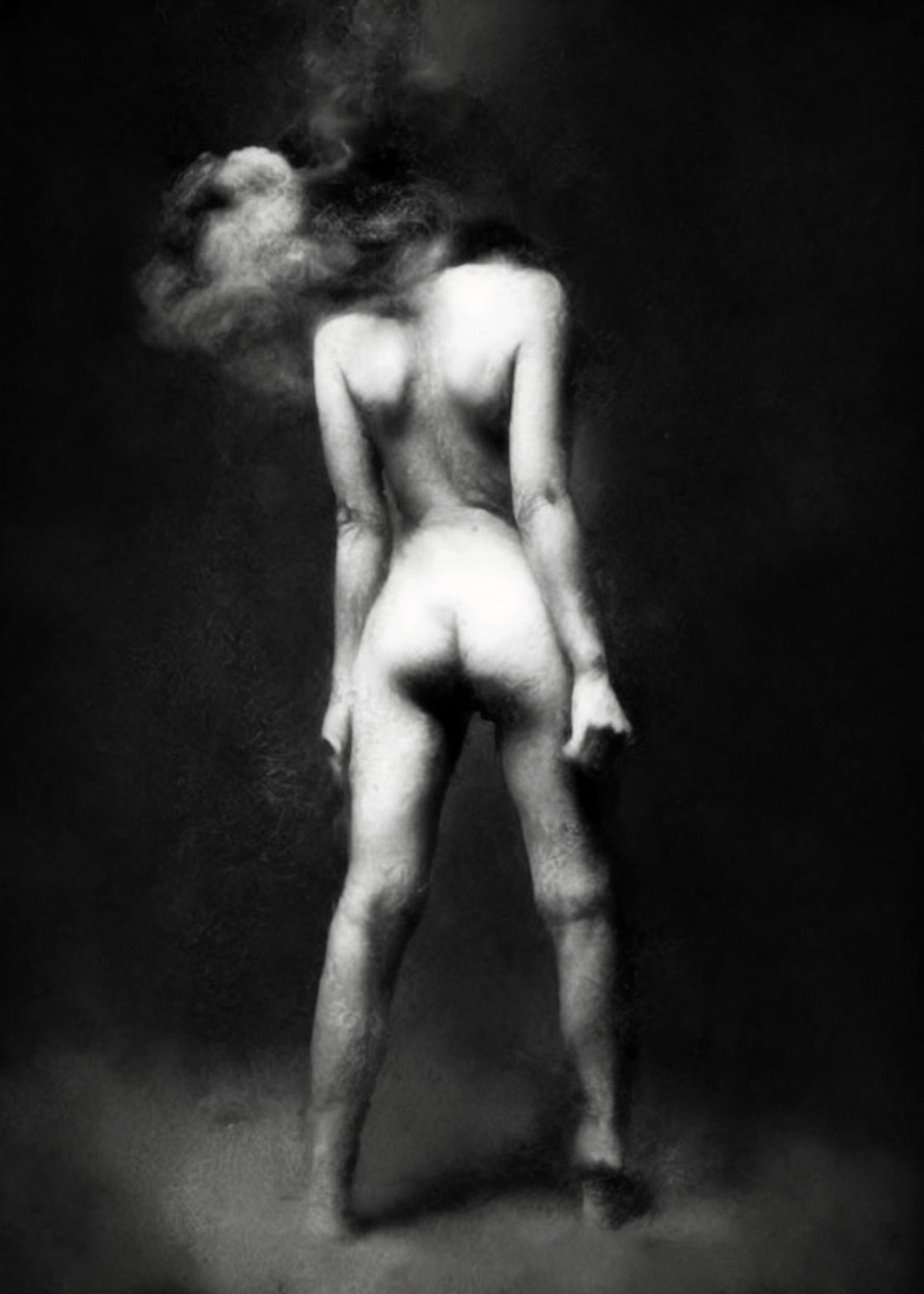 Black and white fine art photograph of a nude female figure seen from behind, with her hair swirling around her head against a dark studio background. Unmoored series.