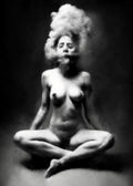 Black and white fine art photograph of a nude female figure sitting cross-legged with her hair styled in a voluminous updo, set against a dark studio background. Unmoored series.