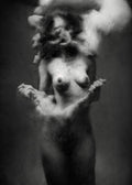 Black and white fine art photograph of a nude female figure with a classical sculpture-like finish, set against a dark studio background. Unmoored series.