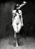 Black and white fine art photograph of a nude female figure standing against a dark textured background, with her head rendered as a surreal melting mass of hair, skin, and abstract forms.  Unmoored series.